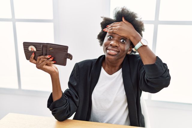 African young woman holding wallet with virtual currency bitcoin stressed and frustrated with hand on head, surprised and angry face