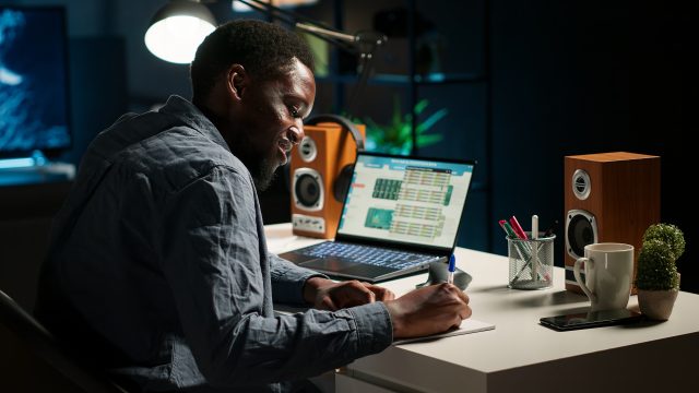 Black freelancer researching online data and writing notes for articles