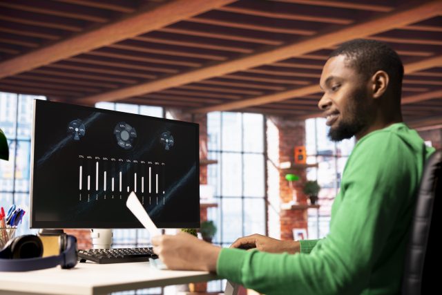 Smiling man in home office using financial application UI on PC screen